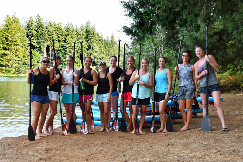 Women standing with SUP Paddles in hand posing for a Group Photo before the Paddle Fit Class begins